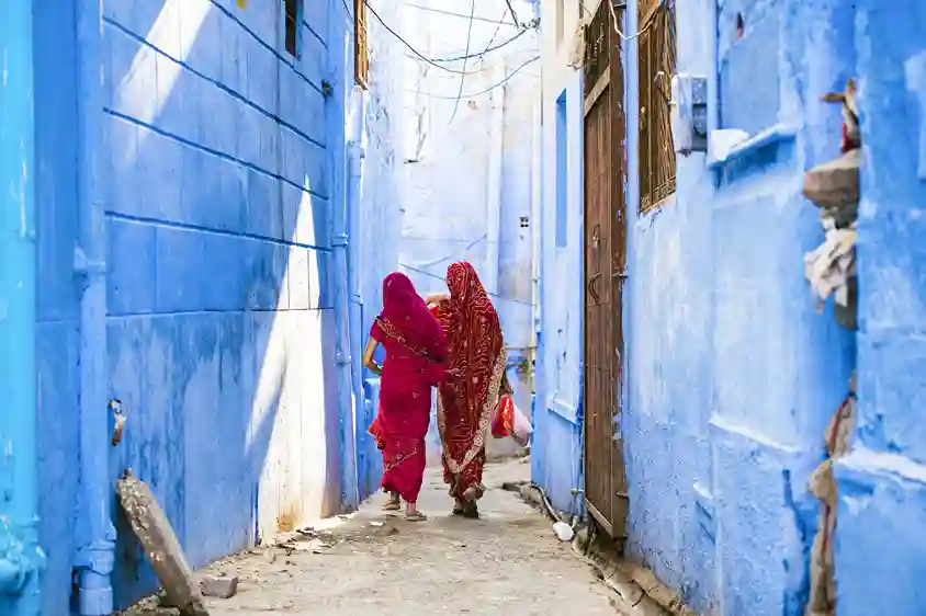 Two women in traditional attire walking through the blue streets of Jodhpur, surrounded by the city's iconic blue walls