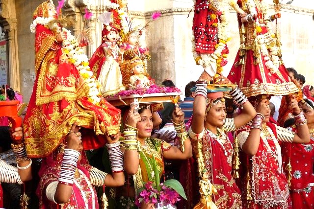 Women beautifully dressed in traditional attire and adorned with ornaments carrying Gangaur idols on their heads during the Gangaur festival celebration.