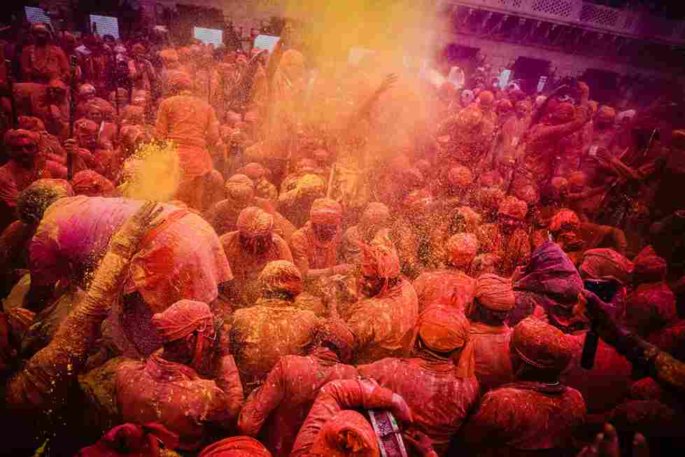 People celebrating Holi festival in Nandgaon, throwing colorful powder and dancing with joy in traditional attire