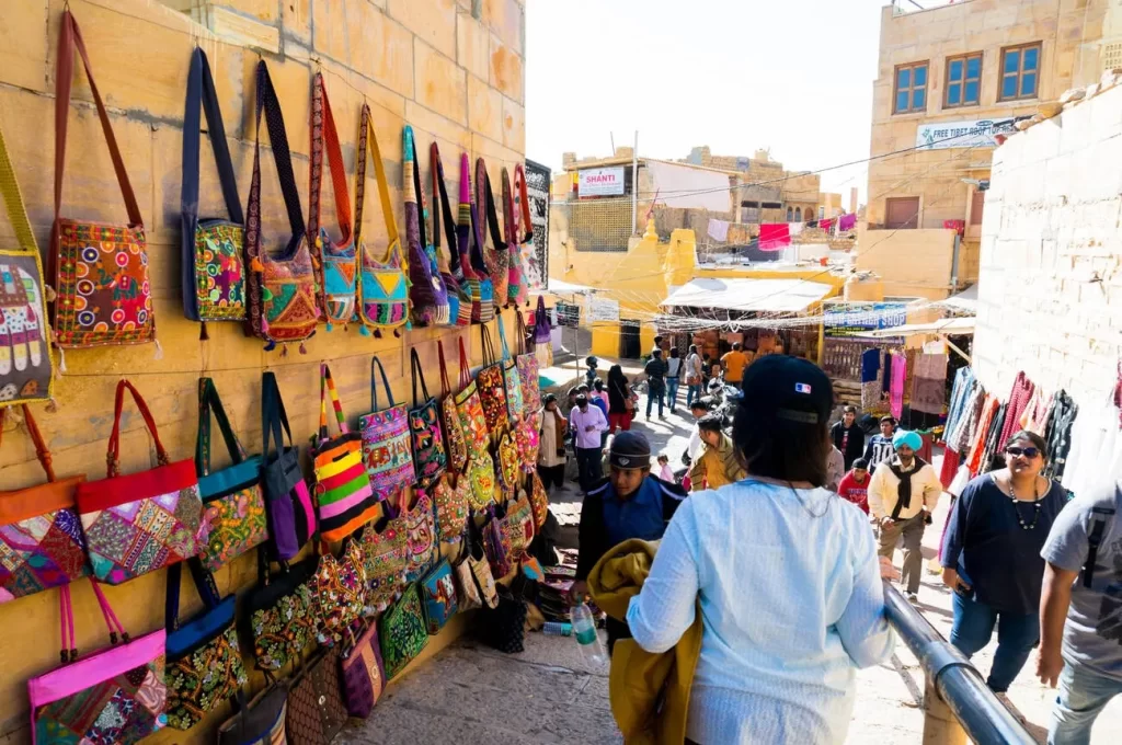 Jaisalmer market scene with bags hung on the wall and people passing by