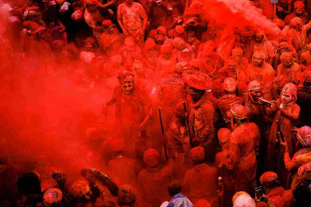 People holding sticks and shields, surrounded by colorful powder, celebrating Holi festival with traditional fervor and enthusiasm