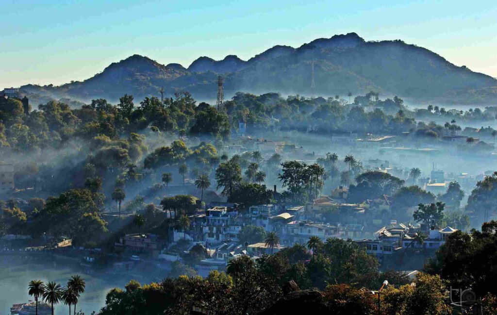 A mist-covered landscape with lush green trees peeking through the fog, creating an enchanting atmosphere in Mount Abu.