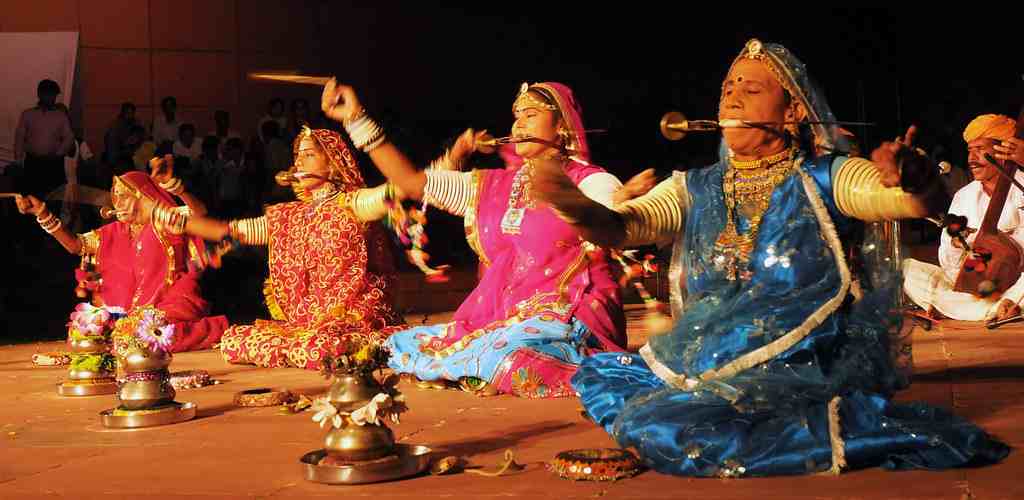 Rajasthani women dressed in vibrant attire gracefully performing a traditional cultural dance on stage, showcasing the rich heritage of Rajasthan.