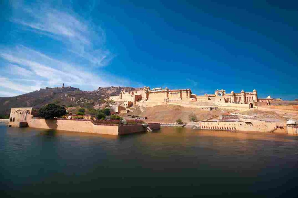 Image of Amer Fort with water in the foreground and hills to the left, capturing the entire fort. Image taken