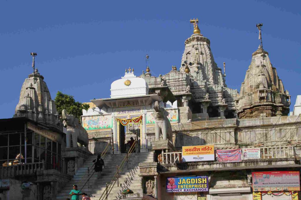 Exterior of Jagdish Temple, Udaipur, Rajasthan, India. Detailed architecture with devotees entering. Surrounding market. Wikimedia Commons.