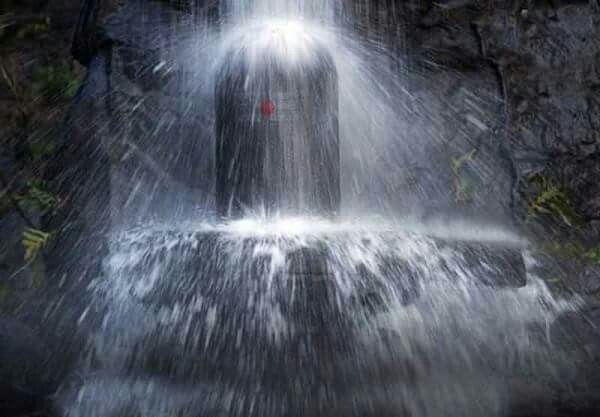 Water cascading rapidly onto a Shiva Lingam, creating a dynamic and energetic visual.