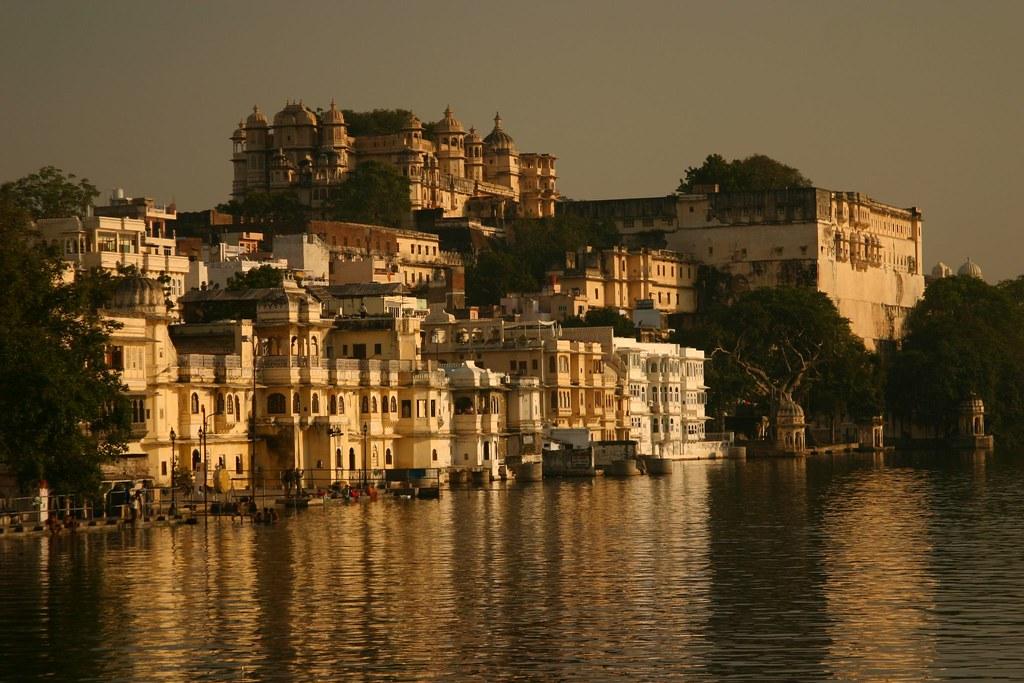 Side view of Bagore Ki Haveli overlooking Lake Pichola, featuring traditional boats in the foreground and palace in the background. Image courtesy: Google.