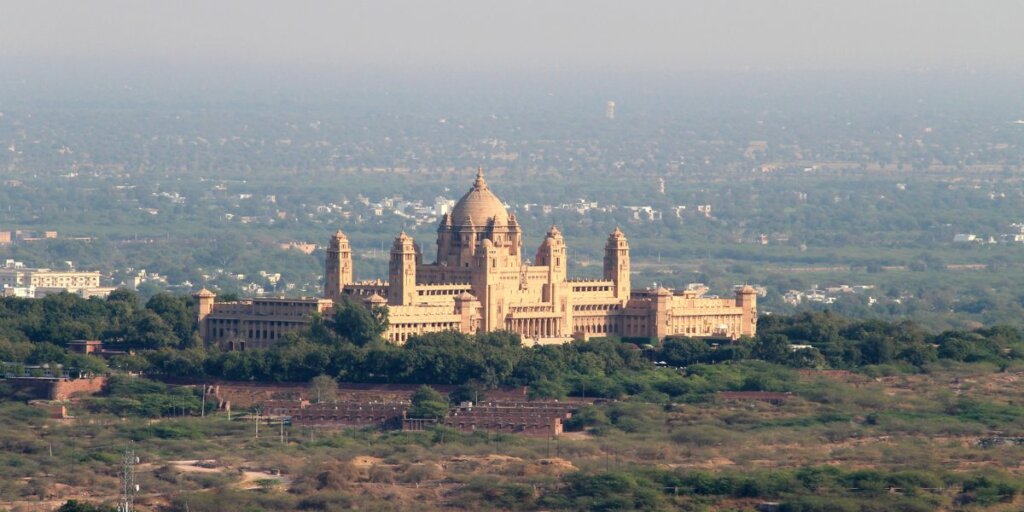 Umaid Bhawan Palace in Jodhpur, Rajasthan, India - a majestic architectural marvel surrounded by lush greenery. Image available on Wikimedia Commons.