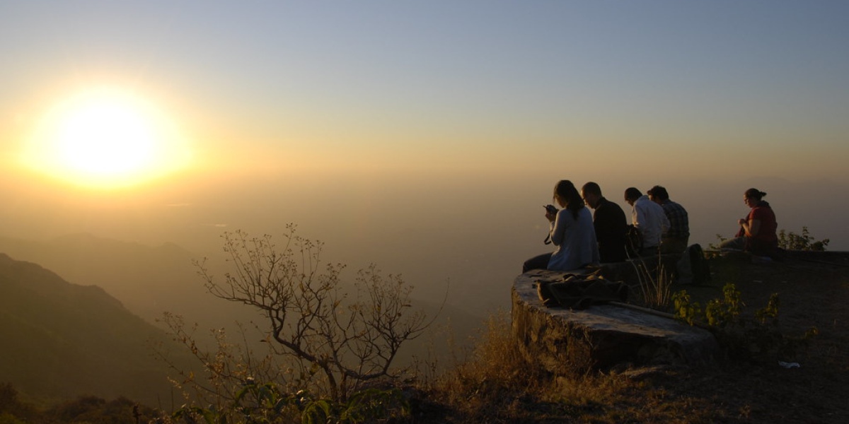 People seated on a cliff edge, watching the sunset, giving the impression that the cliff is suspended in the air with a significant drop below. Image sourced from Flickr.