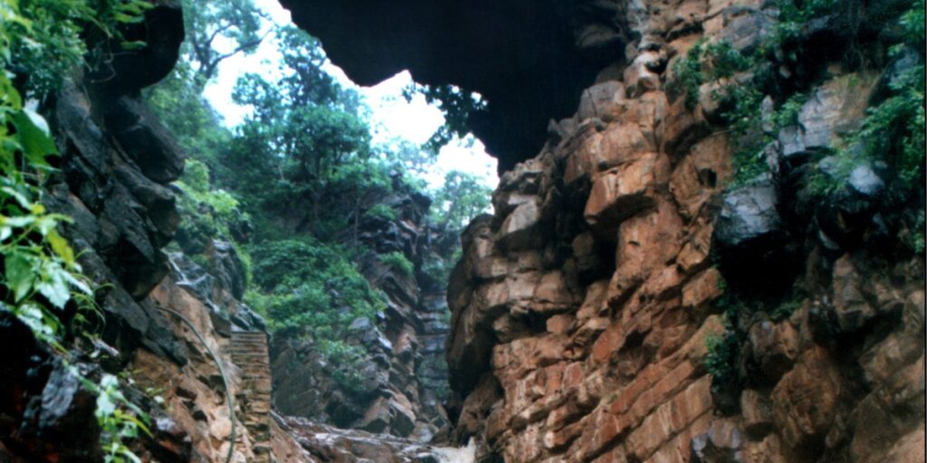 A mountainous landscape with a gateway carved into the rock, representing the scenic beauty of Pandupol, Alwar. Image from Wikimedia."