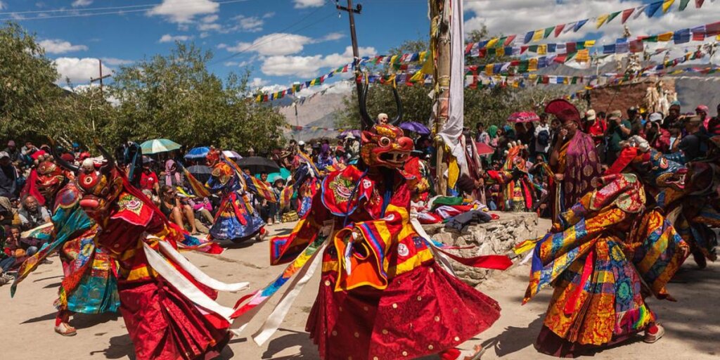 Ladakh festival celebration with traditional dancers performing in vibrant attire, against a backdrop of colorful flags.