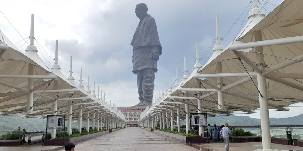 Shaded seating area with benches and umbrellas at the Statue of Unity in Gujarat, providing comfort for visitors exploring the monumental site. Image courtesy: PixaHive.