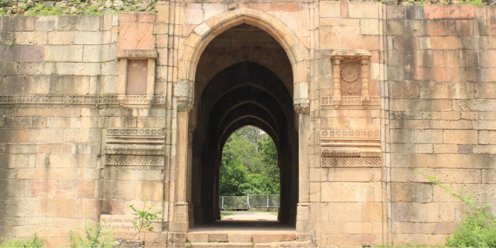 Image of the main entrance gate at Champaner-Pavagadh Archaeological Park in Gujarat. The gate exhibits intricate architectural details against a backdrop of natural greenery. Photo sourced from Wikimedia Commons.