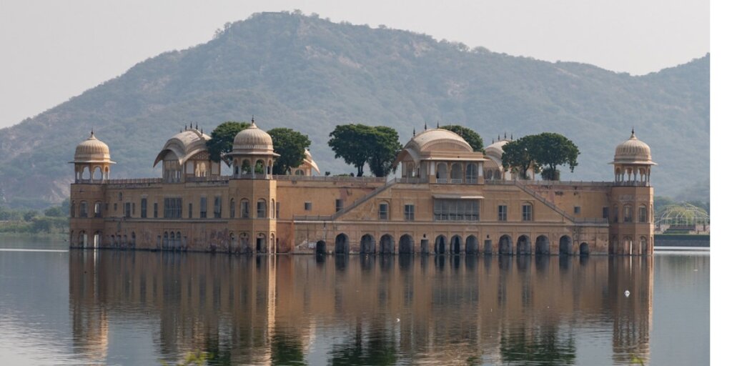 Jal Mahal (Water Palace) in Jaipur, beautifully reflected in the calm waters of Man Sagar Lake during sunset, showcasing its symmetrical Rajput-style architecture and serene surroundings.