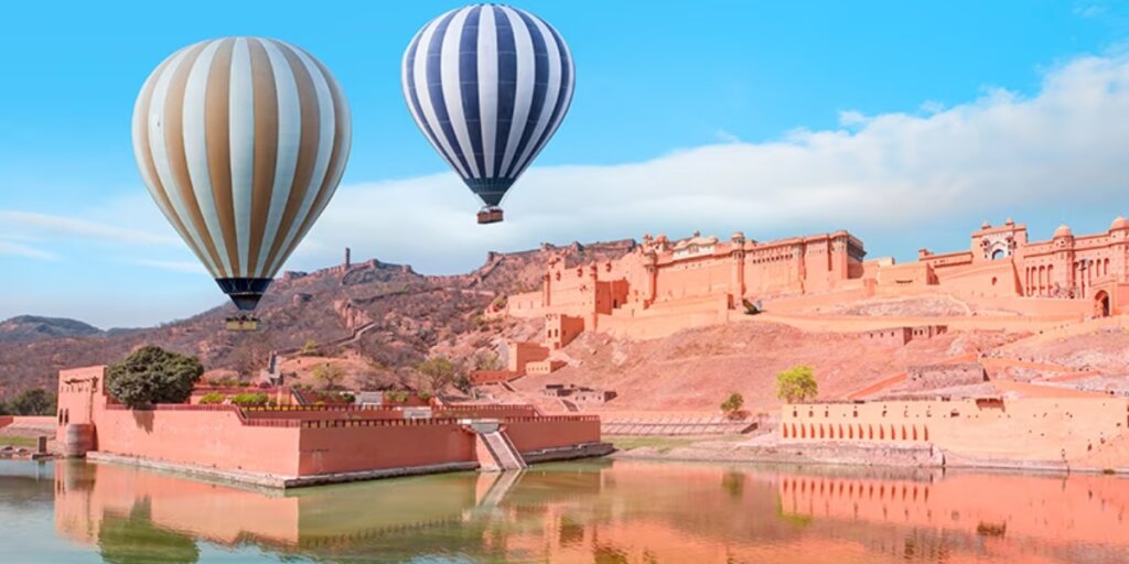 Two hot air balloons floating directly in front of Amer Fort in Jaipur, with the ground and surroundings visible below. Discover the majestic view of Amer Fort from above