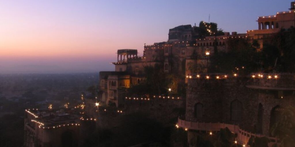 Night view of Neemrana Fort and Palace in Rajasthan, showcasing its illuminated architecture against the dark sky. Image by Flickr.