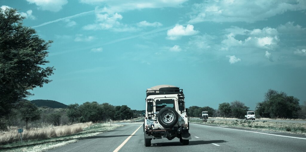 A car travels along a straight highway, framed by expansive views of the countryside under a clear blue sky, depicting a sense of adventure and freedom on a road trip.