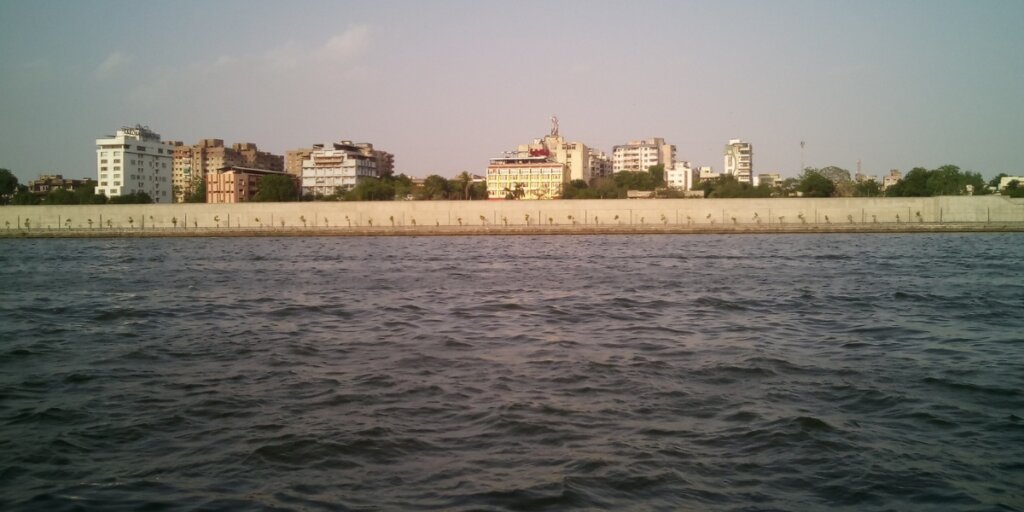 View of the Sabarmati Riverfront in Ahmedabad, featuring the wide, calm river bordered by well-maintained green promenades, bustling with people enjoying leisurely walks and recreational activities under a clear blue sky