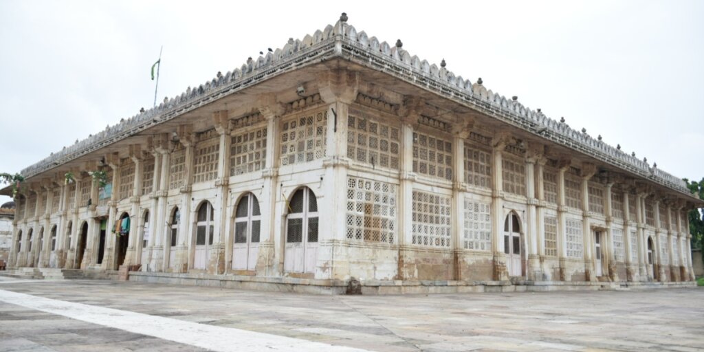 Image of Sarkhej Roza, a mosque and tomb complex in Ahmedabad, Gujarat. The picture showcases the elegant architecture of the buildings amidst serene surroundings. Photo sourced from Wikimedia Commons.