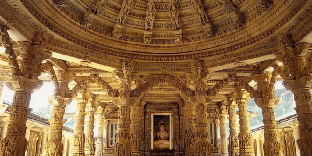 Interior view of Dilwara Jain Temple, Mount Abu, featuring a sculpture of Shri Nemi Nath Ji amidst ornate pillars and intricately carved ceiling