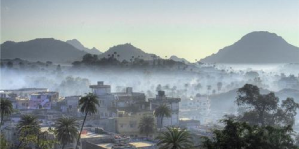 Mount Abu during monsoon with houses partially covered in fog, surrounded by lush greenery and misty hills.