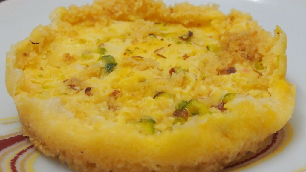 Rajasthani Ghewar: A traditional Indian sweet dish, round in shape with intricate patterns, made from flour and soaked in sugar syrup, garnished with nuts and saffron.