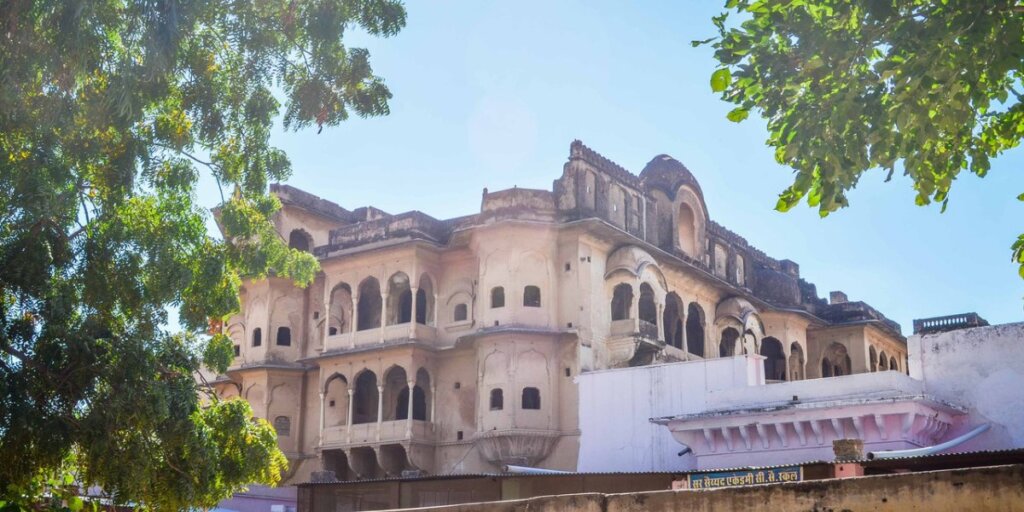 A photo of the Khetri Palace in Jhunjhunu, showing its magnificent architecture with open arches and latticed work. It is also known as the Hawa Mahal of Shekhawati, highlighting its historical and cultural significance.