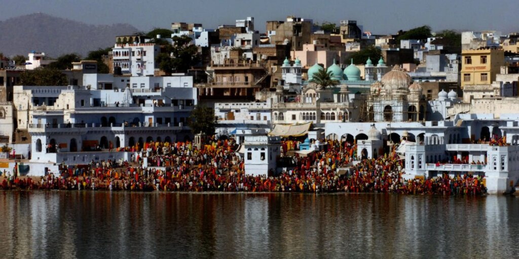 Crowds of people gathered at Pushkar Ghat, engaging in ritual bathing in the sacred waters, with colorful surroundings and traditional attire.